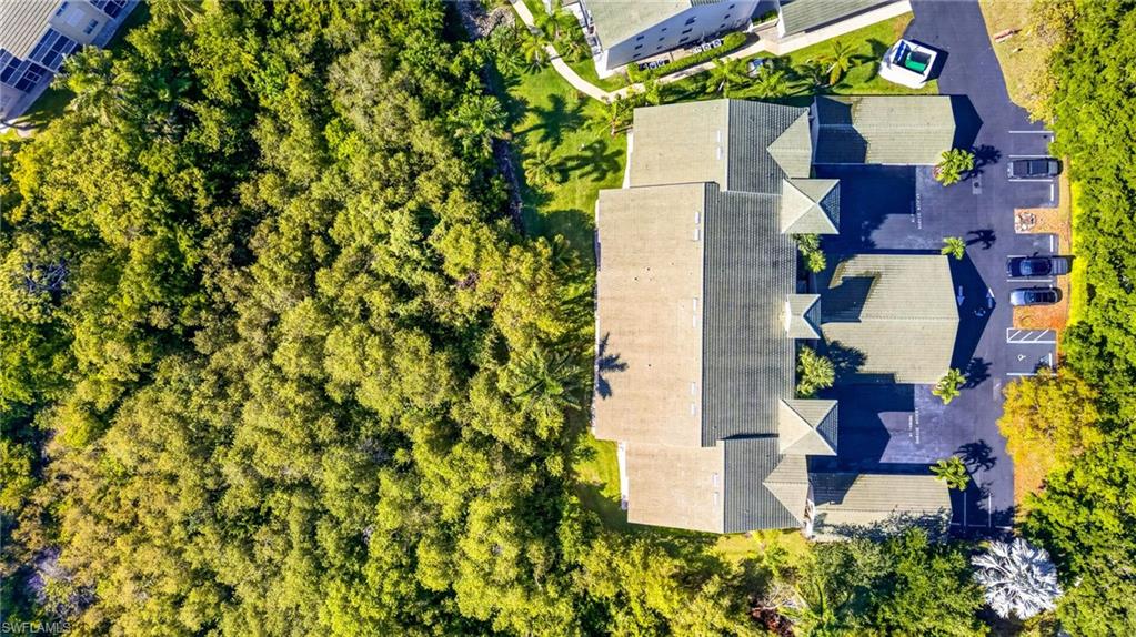 Aerial perspective showcasing the multi-unit residential property featuring a gray shingle roof, asphalt paved parking area, and surrounding mature trees