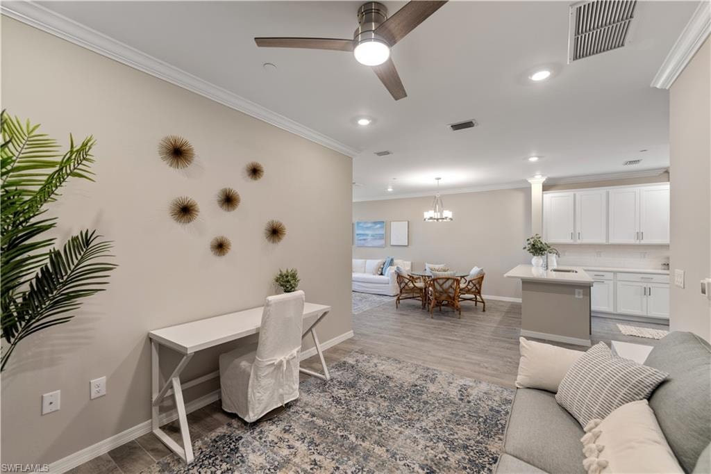 Living room featuring ornamental molding, ceiling fan with notable chandelier, and light hardwood / wood-style floors