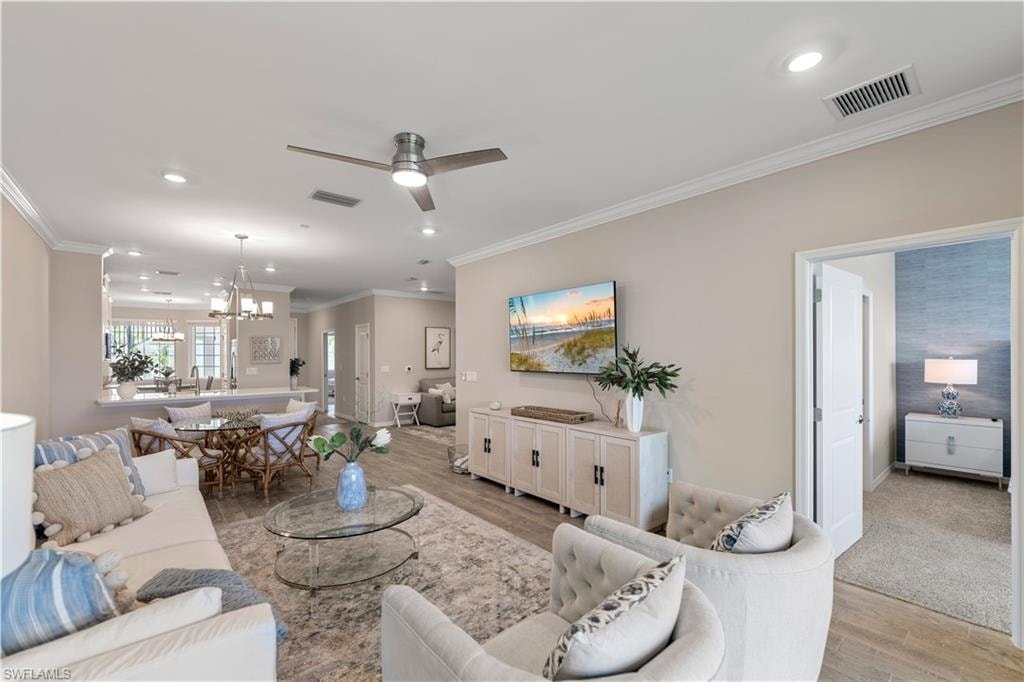 Living room featuring ceiling fan with notable chandelier, crown molding, and light wood-type flooring