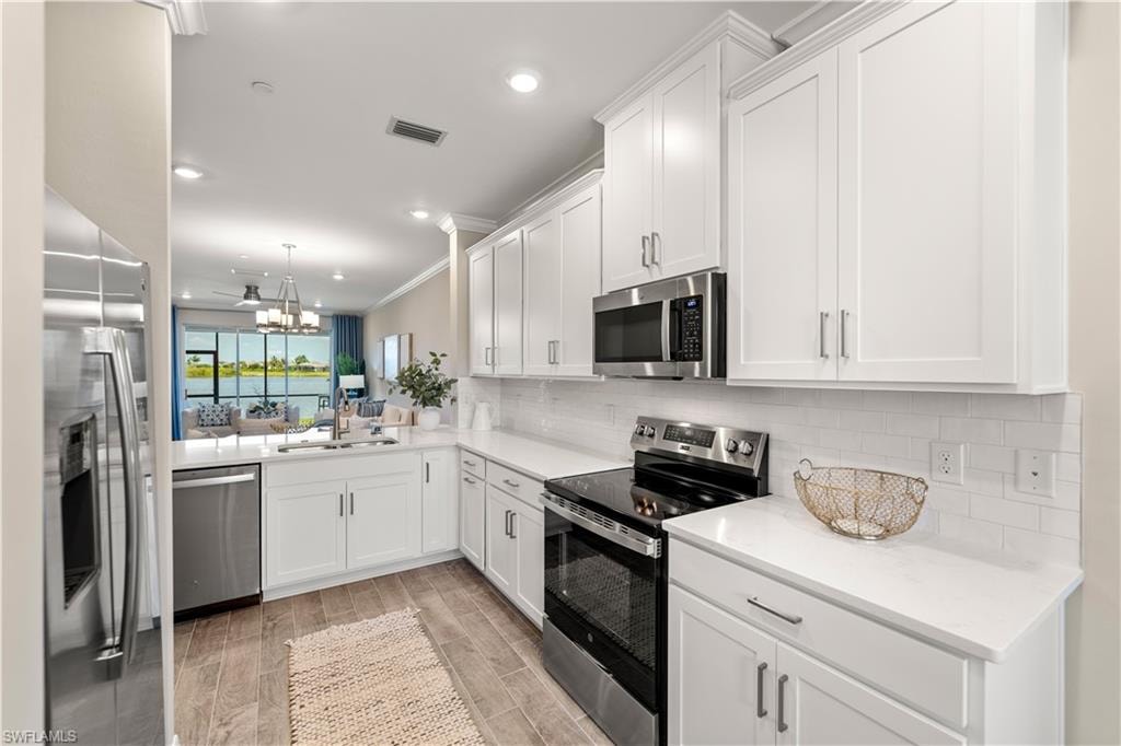 Kitchen featuring appliances with stainless steel finishes, tasteful backsplash, white cabinets, sink, and light hardwood / wood-style floors