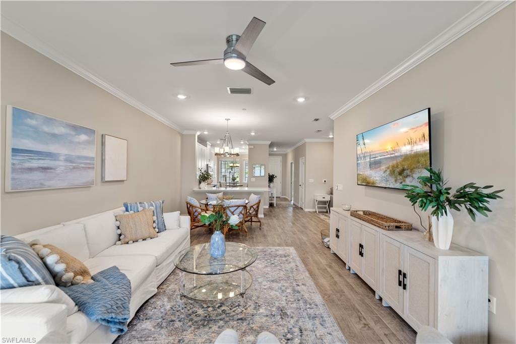 Living room featuring light hardwood / wood-style floors, ornamental molding, and ceiling fan with notable chandelier