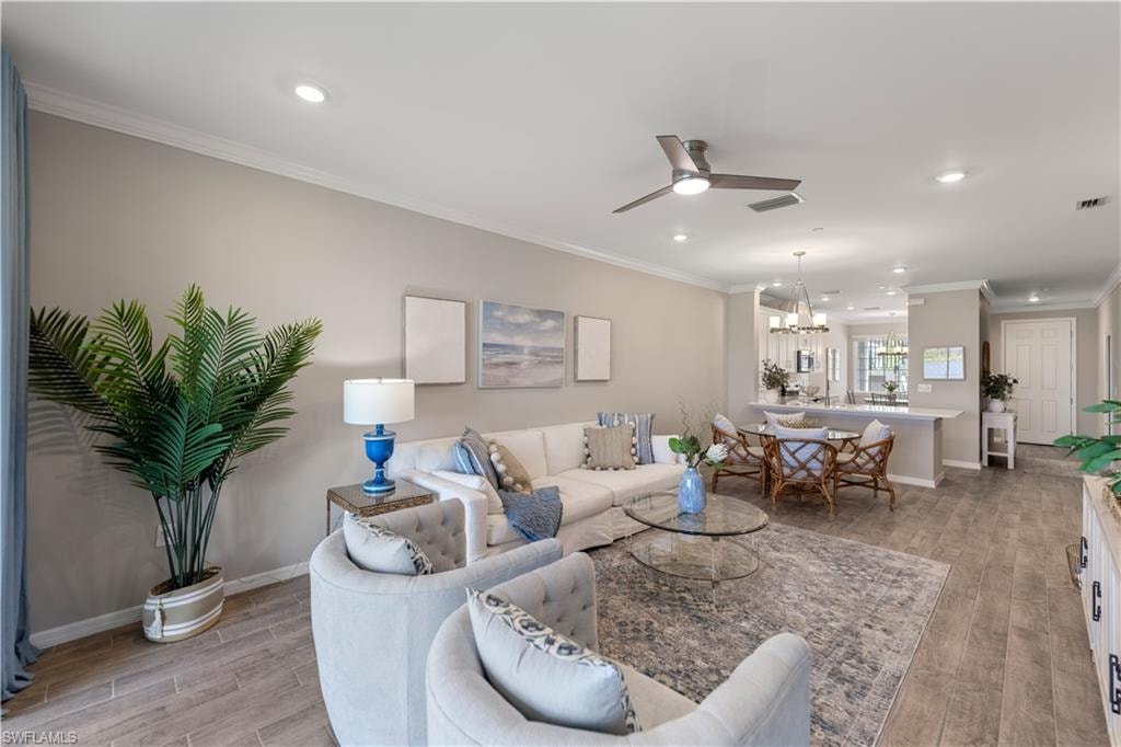 Living room featuring crown molding, light wood-type flooring, and ceiling fan with notable chandelier