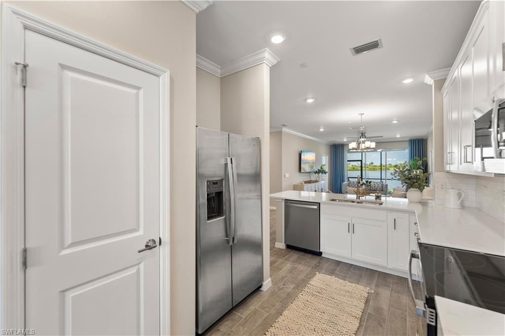 Kitchen with white cabinetry, crown molding, kitchen peninsula, dark hardwood / wood-style floors, and appliances with stainless steel finishes