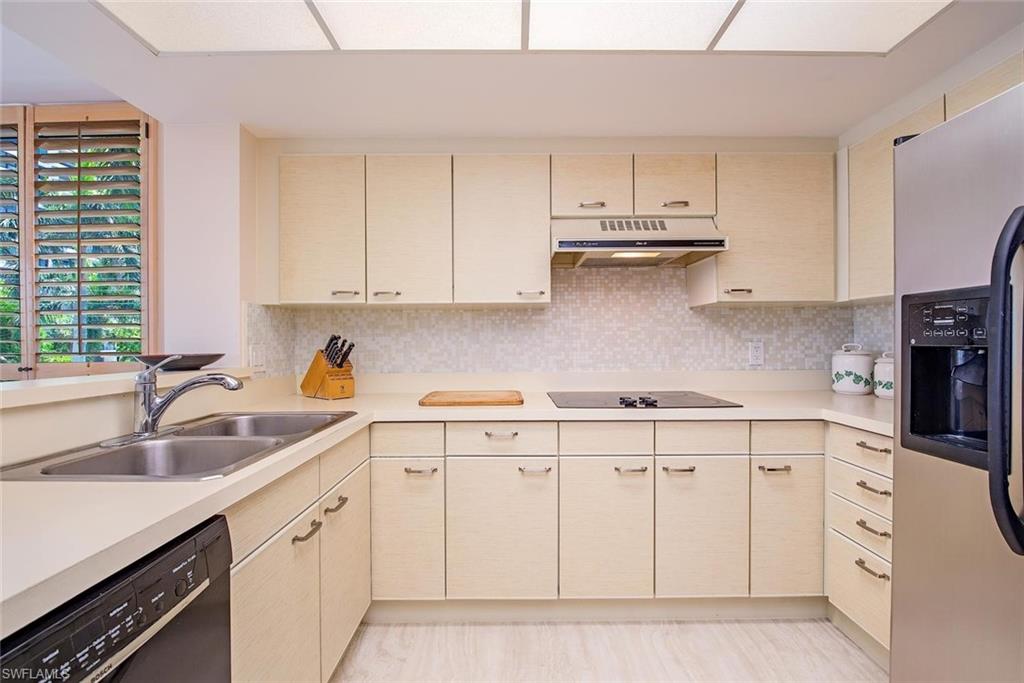 Kitchen featuring a double basin stainless steel sink, light wood-finish cabinetry, a built-in electric cooktop, and a mosaic tile backsplash