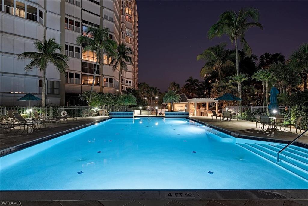 Illuminated swimming pool with integrated steps, surrounded by mature palm trees and tropical landscaping
