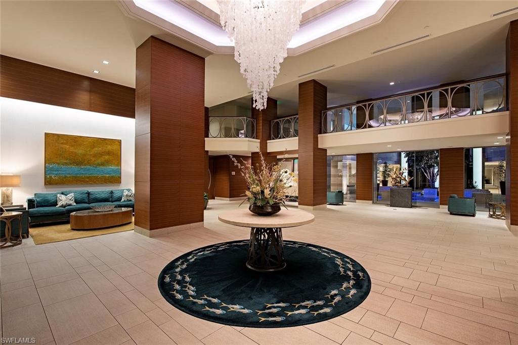 Spacious lobby featuring a grand chandelier, light-toned tile flooring, rich wood-paneled columns, and a decorative balcony with intricate railings