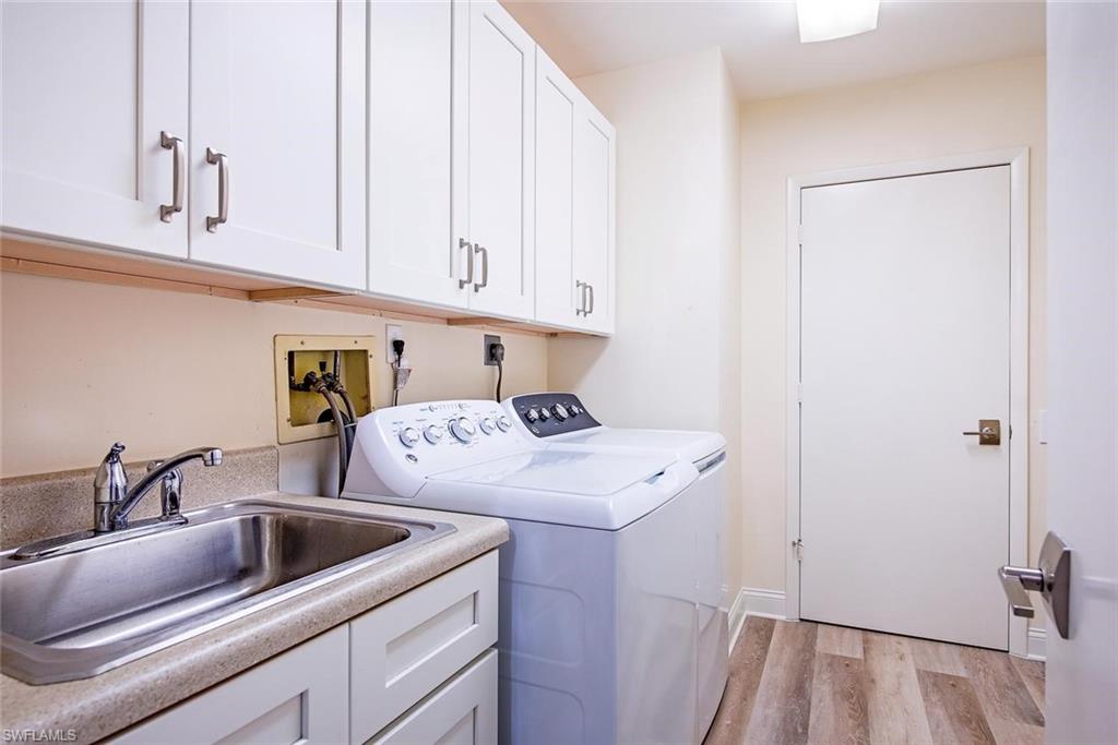 Dedicated laundry space featuring white shaker cabinetry, an integrated utility sink, wood-finish flooring, a neutral countertop, and brushed nickel hardware
