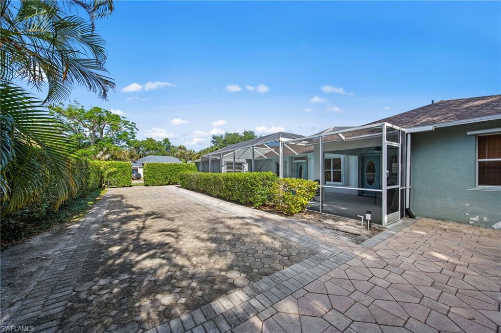 Paver driveway bordered by manicured hedges, leading to a screened patio entry