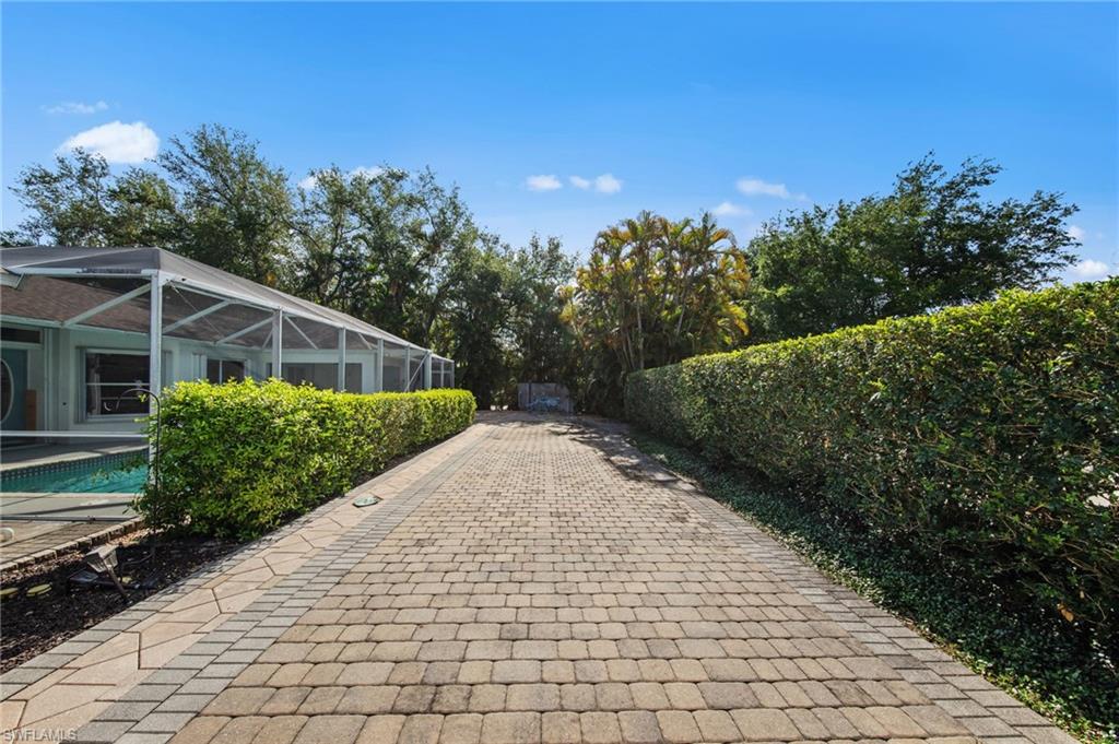 Paved driveway with paver stone border, bordered by mature hedges on both sides