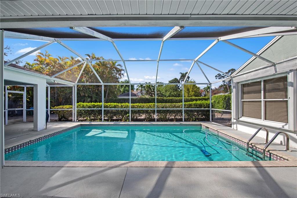 Screened outdoor pool area featuring a rectangular pool with tiled border, concrete surround, and steps with handrails