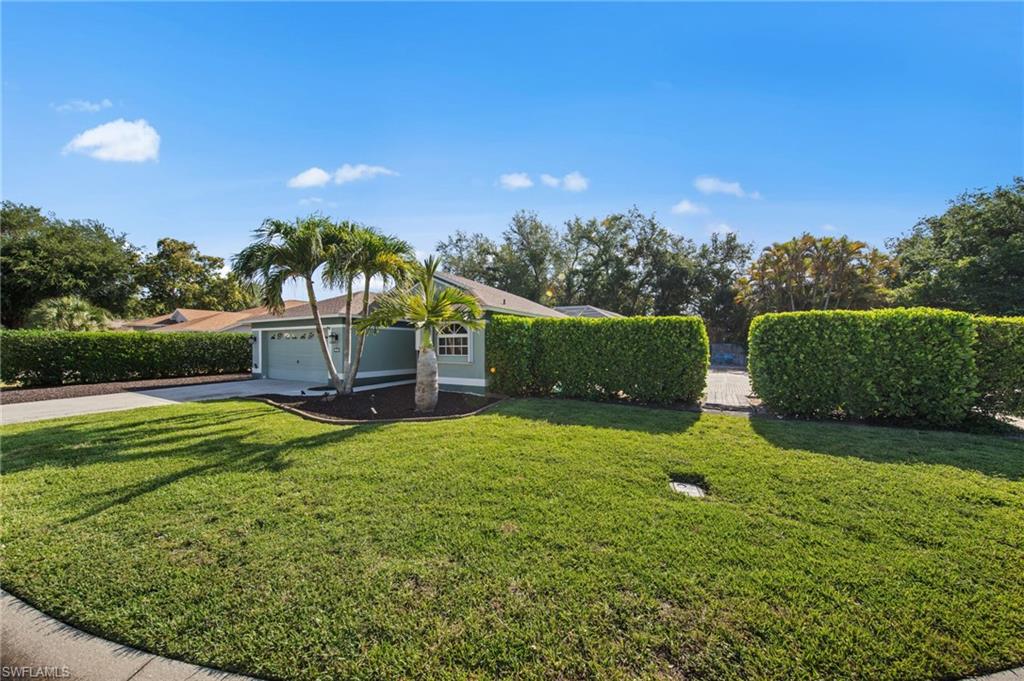Single-story residence featuring a two-car garage, mature palm trees, and established perimeter hedges