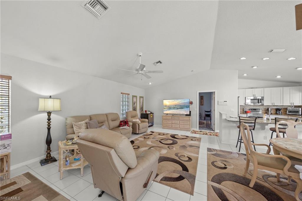 Open-concept living area featuring white tile flooring, vaulted ceilings, a ceiling fan, and recessed lighting