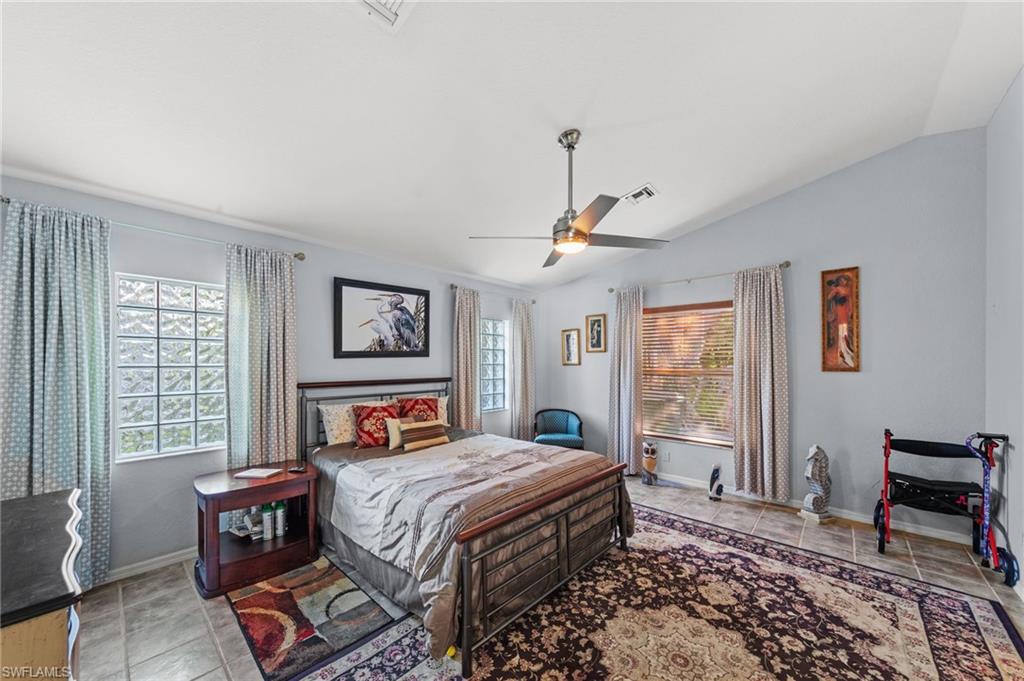 Spacious room featuring vaulted ceilings, tile flooring, a ceiling fan with integrated lighting, and multiple windows including glass block accents