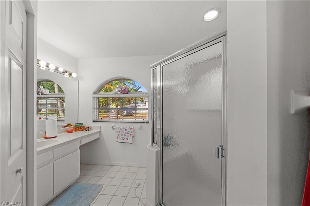 Bathroom featuring a glass-enclosed shower, white tile flooring, a dual-basin vanity with ample counter space, and arched windows