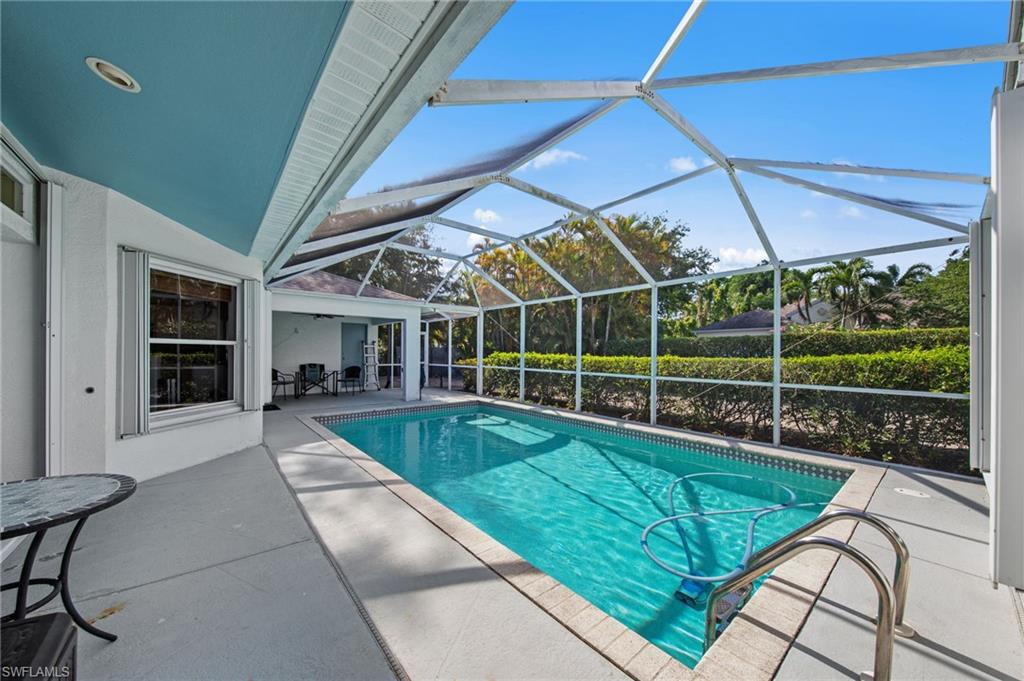Screened pool enclosure featuring a rectangular swimming pool with tile coping, integrated pool steps, and a surrounding concrete patio