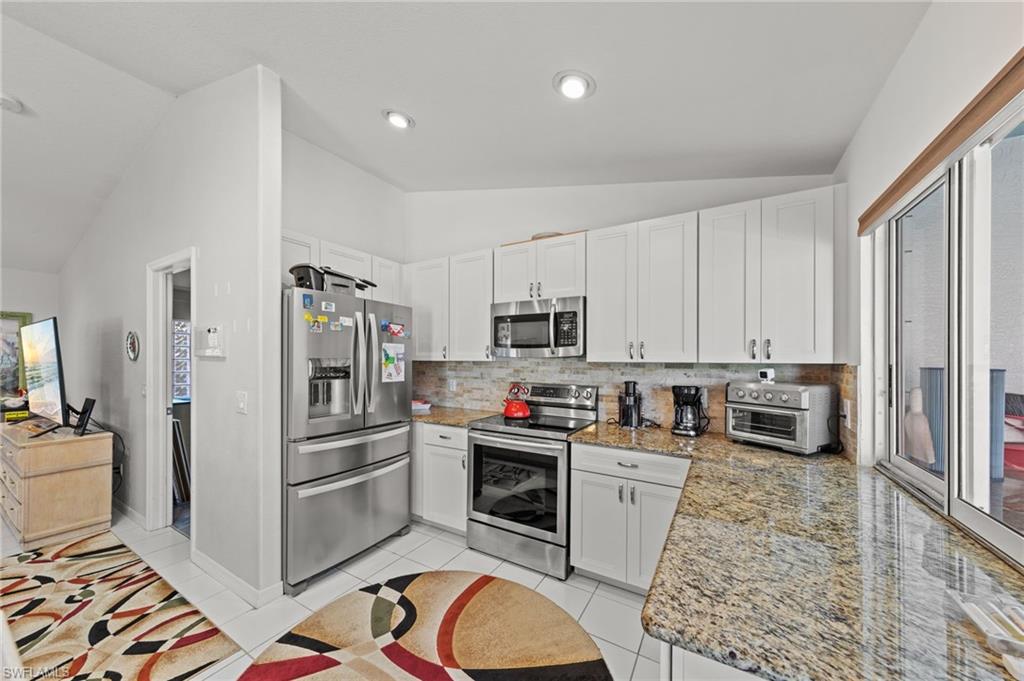 Kitchen featuring granite countertops, stainless steel appliances, white cabinetry, a tile backsplash, and a sliding glass door