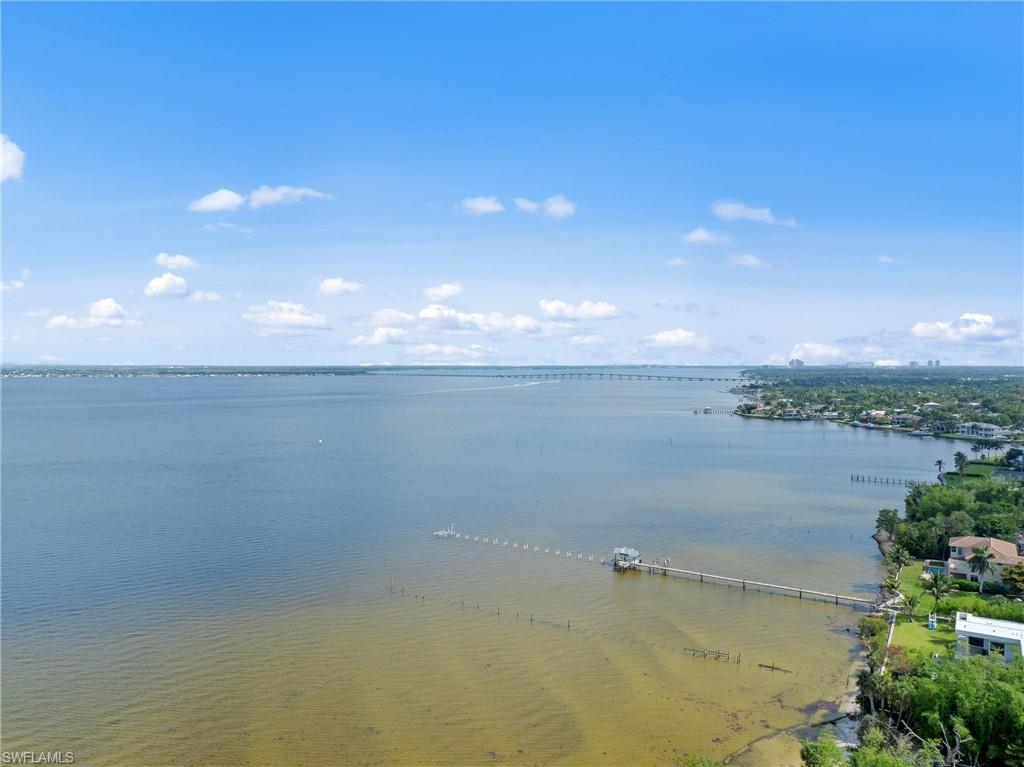 Expansive waterfront setting featuring a private dock with covered boat lift, surrounded by lush green landscaping