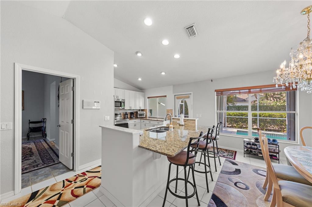 Kitchen featuring white cabinetry, granite countertops, an island with bar seating, and a large window overlooking a pool area