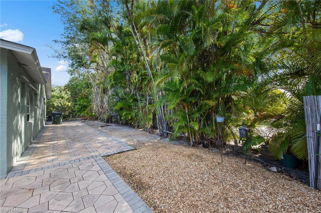Paver pathway extending alongside the property, bordered by a gravel area and mature tropical landscaping