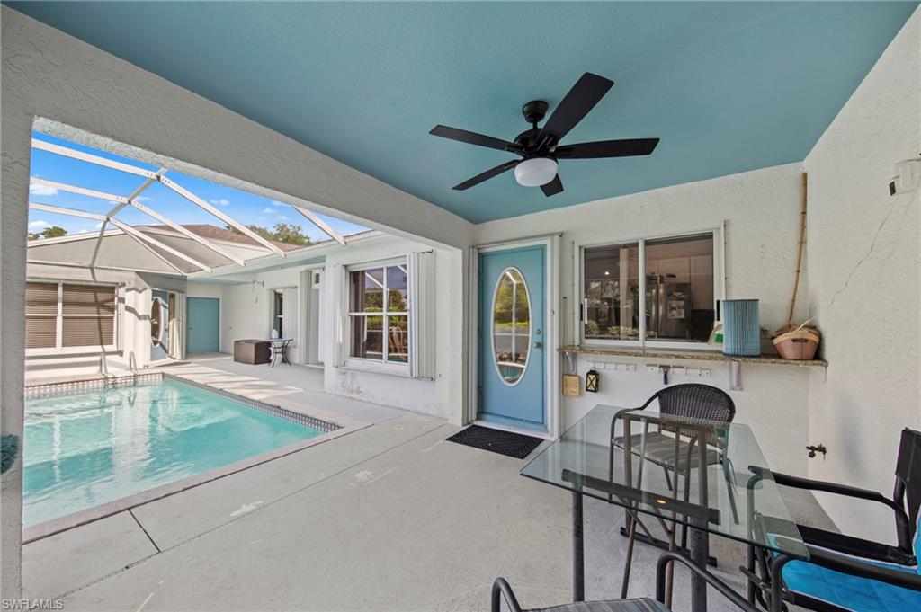 Screened-in pool deck featuring a swimming pool with tile accents, an overhead fan, a solid blue entry door with an oval glass insert, a granite-finish bar area, and a light blue ceiling
