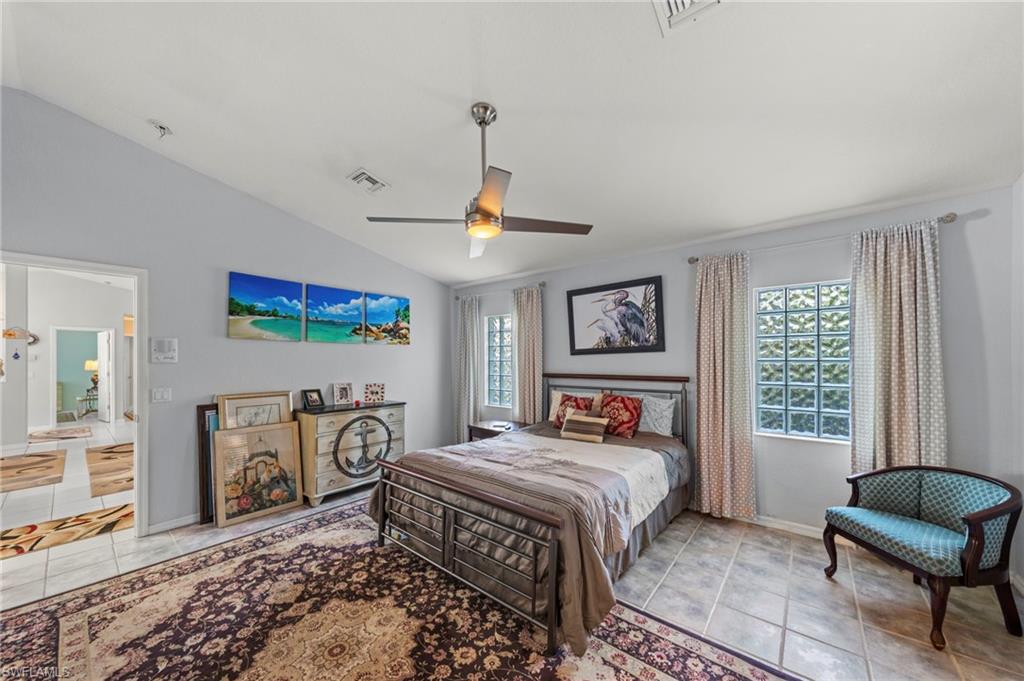 Vaulted ceiling bedroom featuring a ceiling fan with integrated lighting, ceramic tile flooring, and glass block windows providing natural light