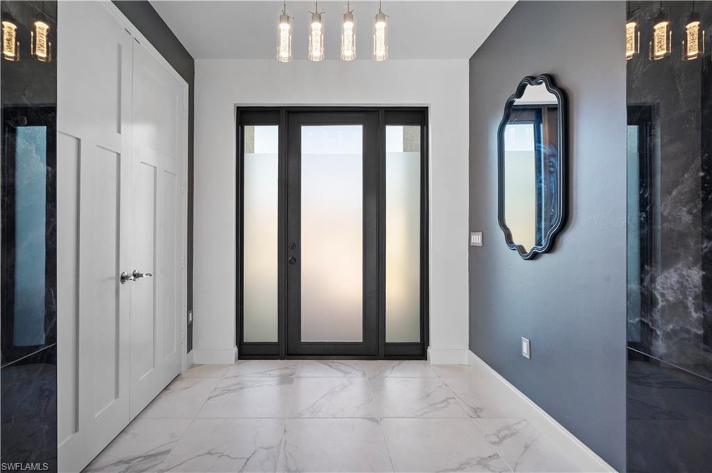 Entryway featuring a frosted glass door with black framing, white panel doors, overhead pendant lighting, and light-toned tile flooring