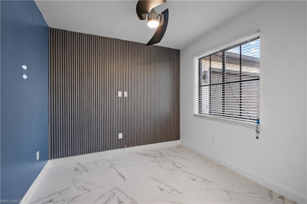 Accent wall with vertical paneling, large window with blinds, ceiling fan, and white baseboards