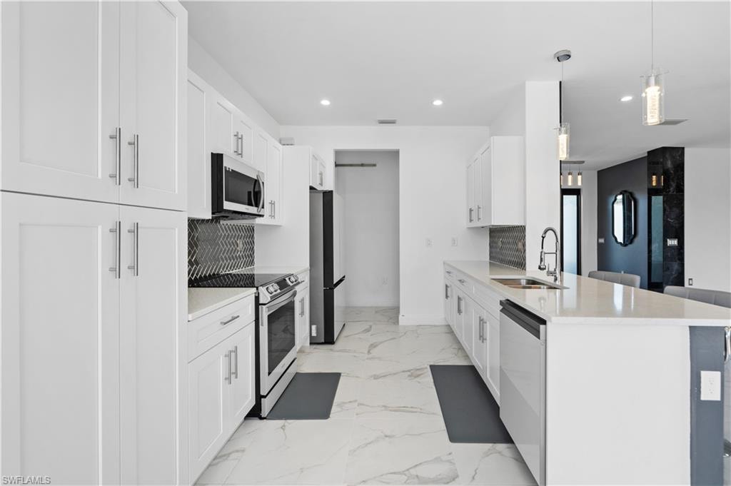 Modern kitchen featuring white shaker-style cabinetry, stainless steel appliances, a geometric tile backsplash, and light-toned countertops