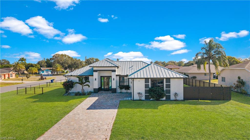 Contemporary-style residence featuring a prominent metal roof, a paver driveway, and a manicured lawn