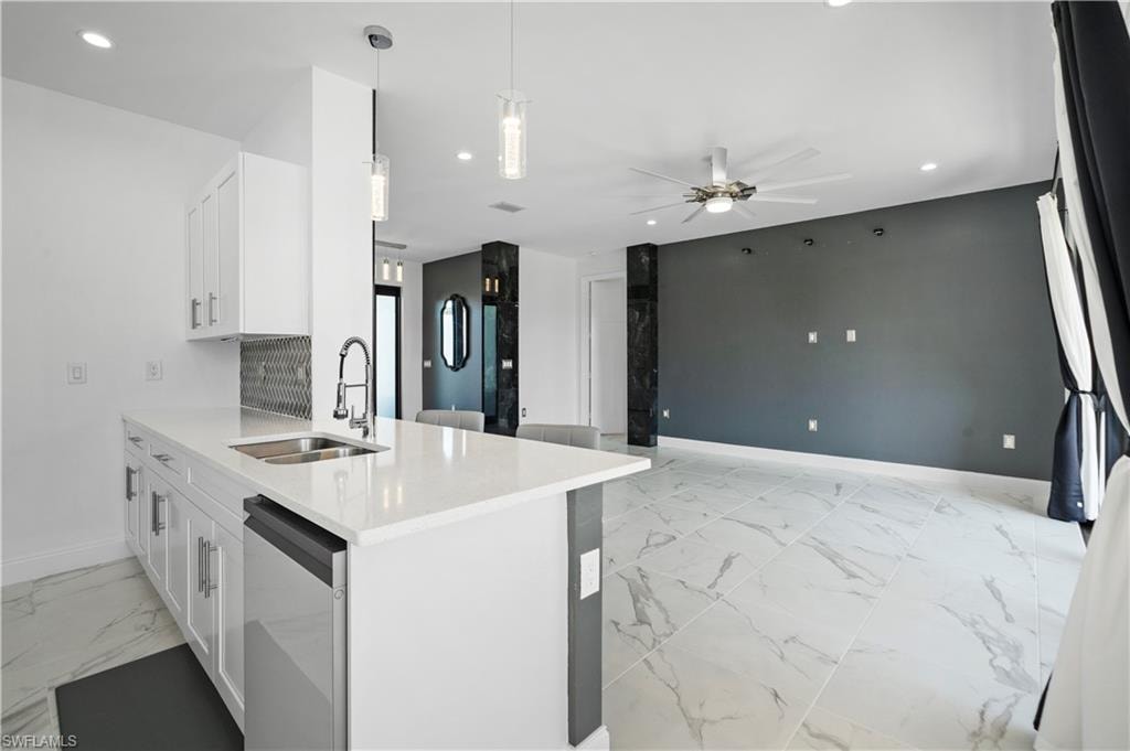 Open-concept living space featuring a kitchen island with a double basin sink, white shaker cabinetry, quartz countertops, and a patterned tile backsplash