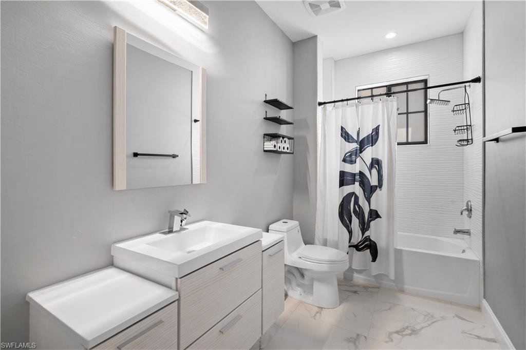 Bathroom featuring a modern vanity with integrated sink, white marble-look flooring, built-in bathtub, and horizontal white tile wall surround