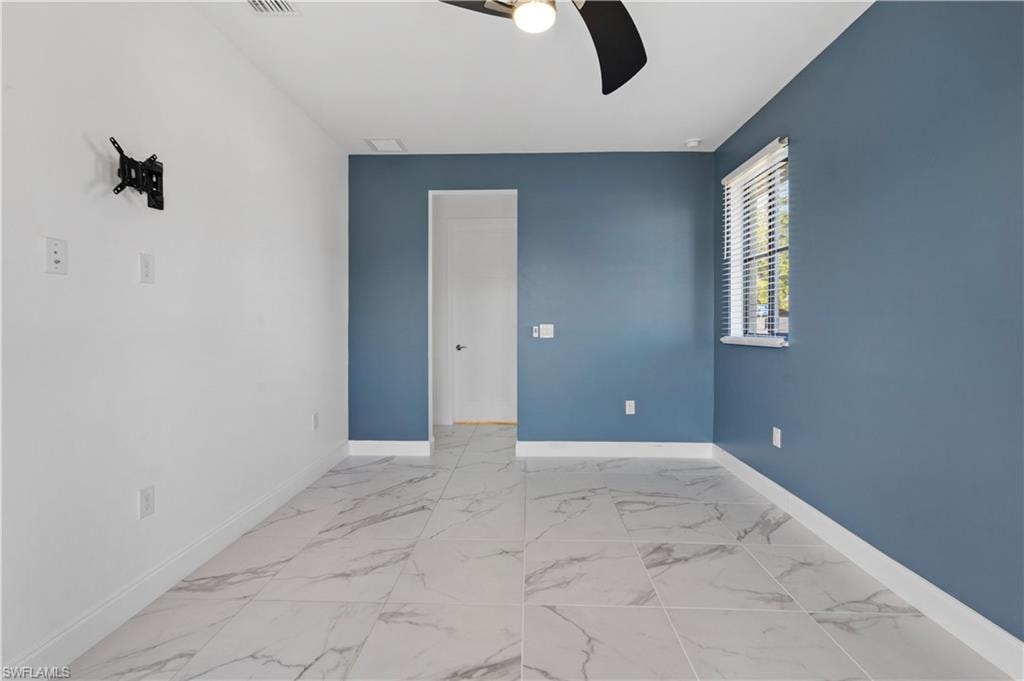 Spacious room featuring large format tile flooring, a window with horizontal blinds, a ceiling fan, and a wall-mounted television bracket