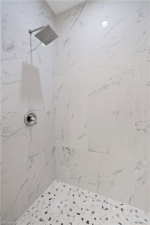 Shower with large format white and gray veined wall tiles, a square rainfall shower head, and a pebble-style floor