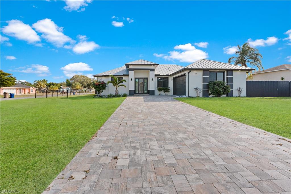 Contemporary residence featuring a paver driveway, white stucco exterior, dark trim accents, a metal roof, and a two-car garage