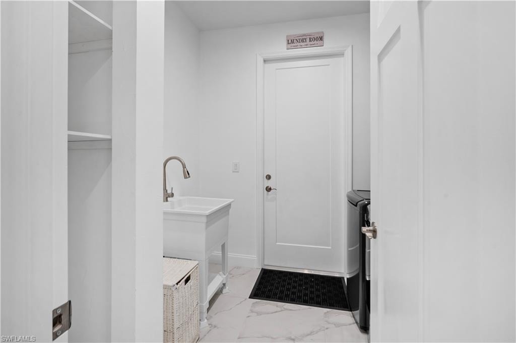 Laundry room featuring a white utility sink with a gooseneck faucet, marble-look floor tiles, and a built-in shelving unit