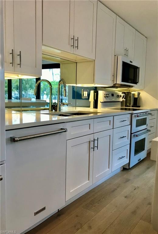 Kitchen with white cabinets, range with two ovens, light countertops, light wood-style floors, and a sink