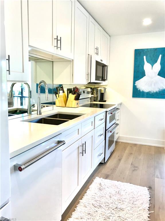 Kitchen featuring white cabinets, dishwashing machine, light countertops, double oven range, and a sink
