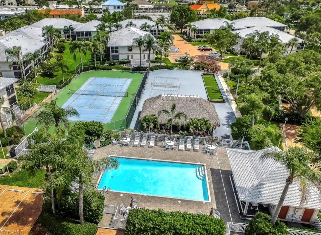Outdoor swimming pool with surrounding lounge chairs, a covered tiki-style structure, and a tennis court