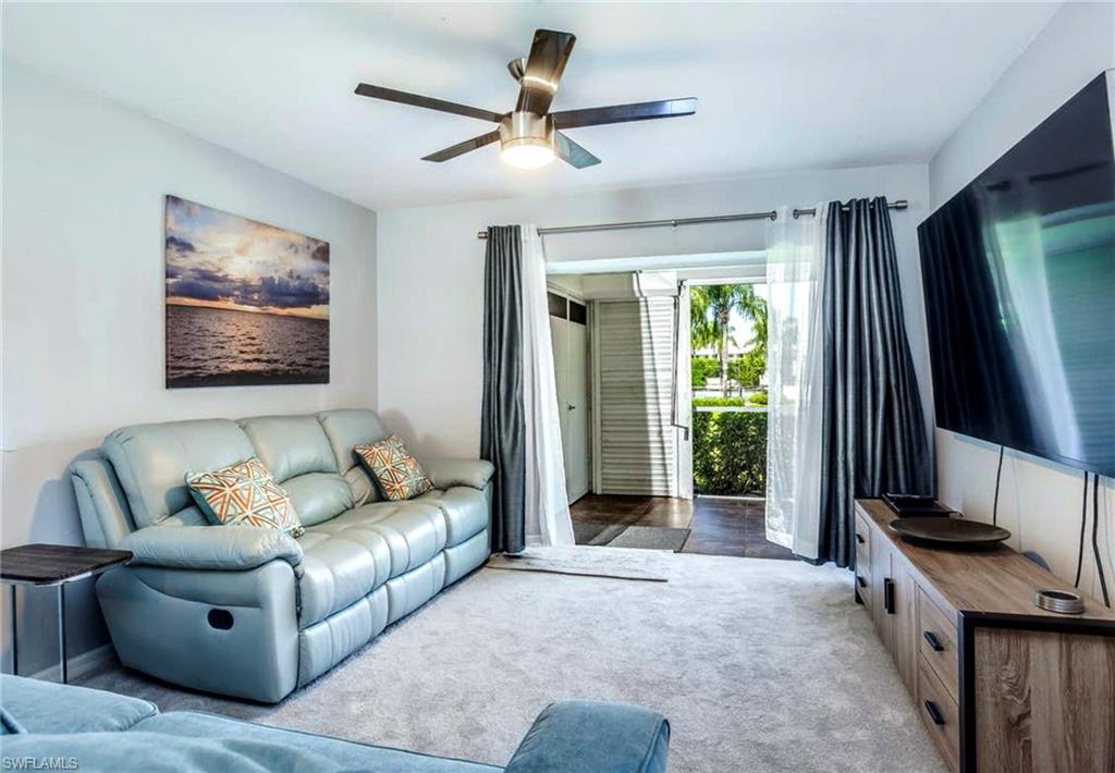Living area featuring light-toned carpeting, a ceiling fan with integrated lighting, and a wall-mounted flat-screen display