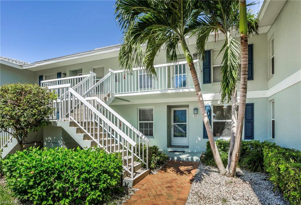 Exterior entry featuring brick paver walkway, mature palm trees, and lush landscaping
