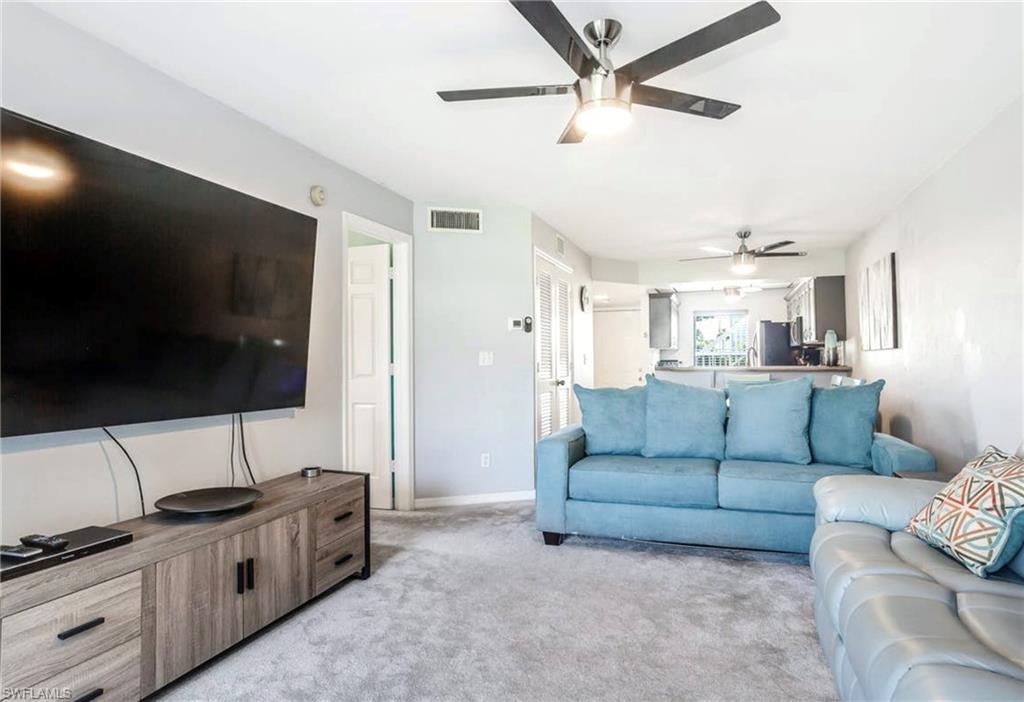 Bright living area featuring light gray walls, plush gray carpeting, and dual ceiling fans with integrated lighting