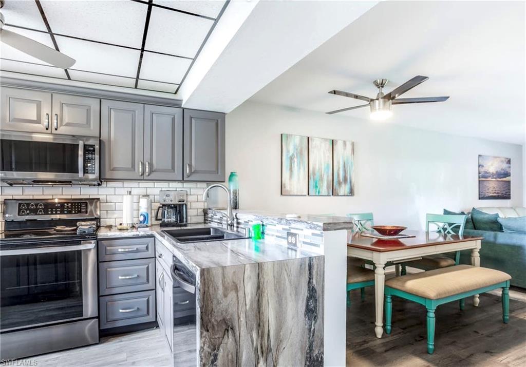 Kitchen featuring grey shaker-style cabinetry, stainless steel appliances, white subway tile backsplash, and a waterfall-edge countertop