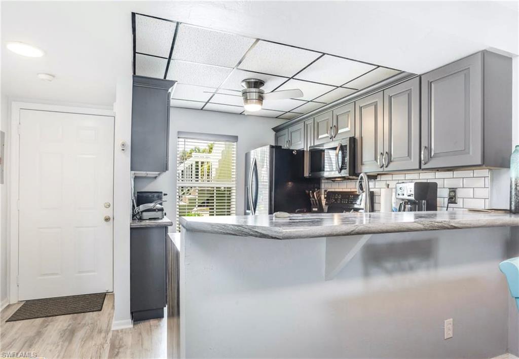 Kitchen featuring gray shaker-style cabinetry, a white subway tile backsplash, and a light-toned countertop with a breakfast bar