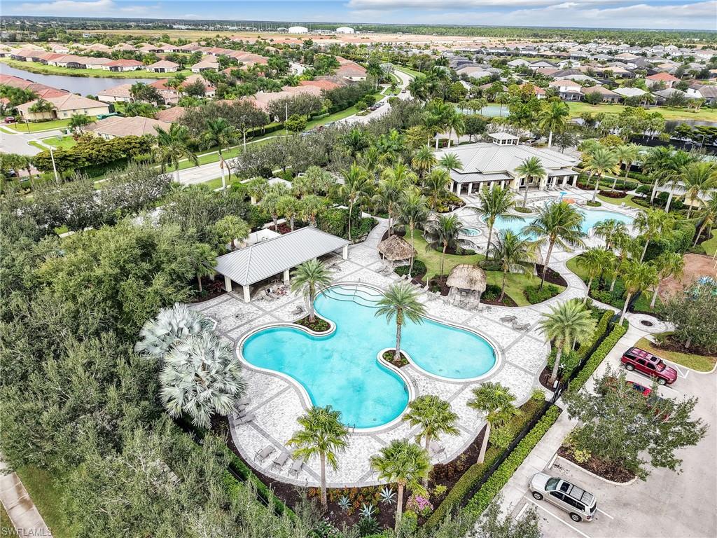 Expansive community amenity center featuring two freeform pools, a large clubhouse, two covered pavilions, and extensive tropical landscaping with mature palm trees