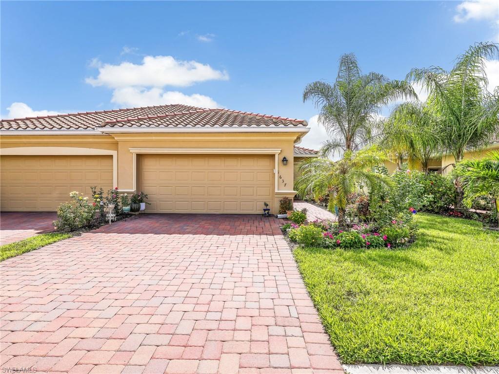 Exterior featuring a terracotta tile roof, two garage bays, a paver driveway, mature palm trees, and established landscaping