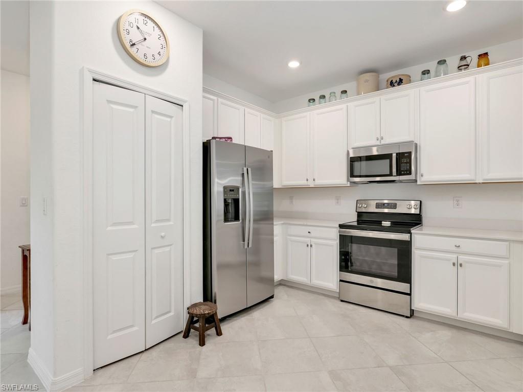 Corner kitchen featuring white cabinetry, light-toned countertops, stainless steel appliances, recessed lighting, and large format tile flooring