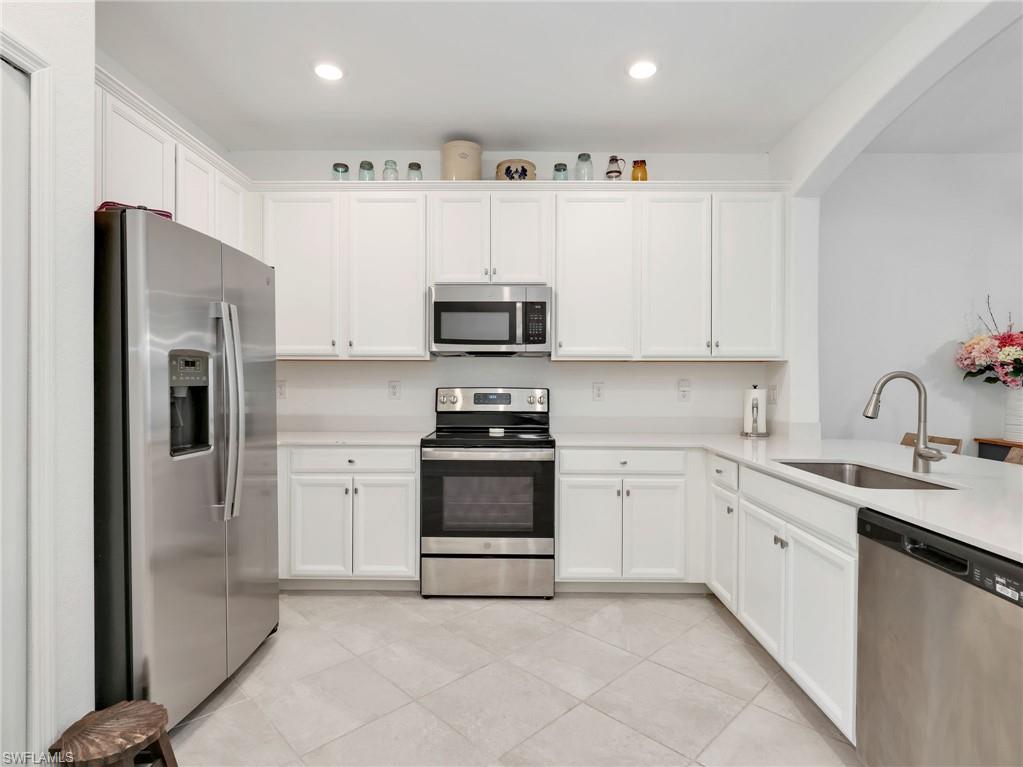 Kitchen featuring white shaker-style cabinetry, light-toned countertops, and stainless steel appliances including a refrigerator, range, microwave, and dishwasher