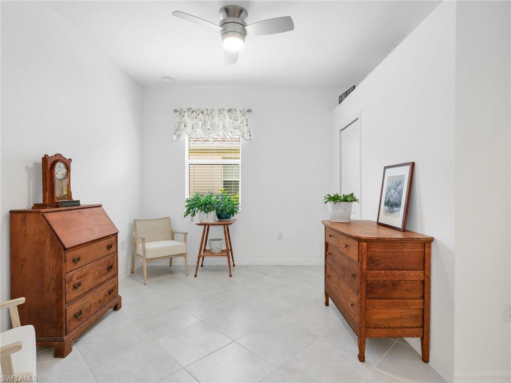 Bright interior space featuring light-toned tile flooring, a window with blinds and valance, high ceilings, and a ceiling fan with integrated lighting
