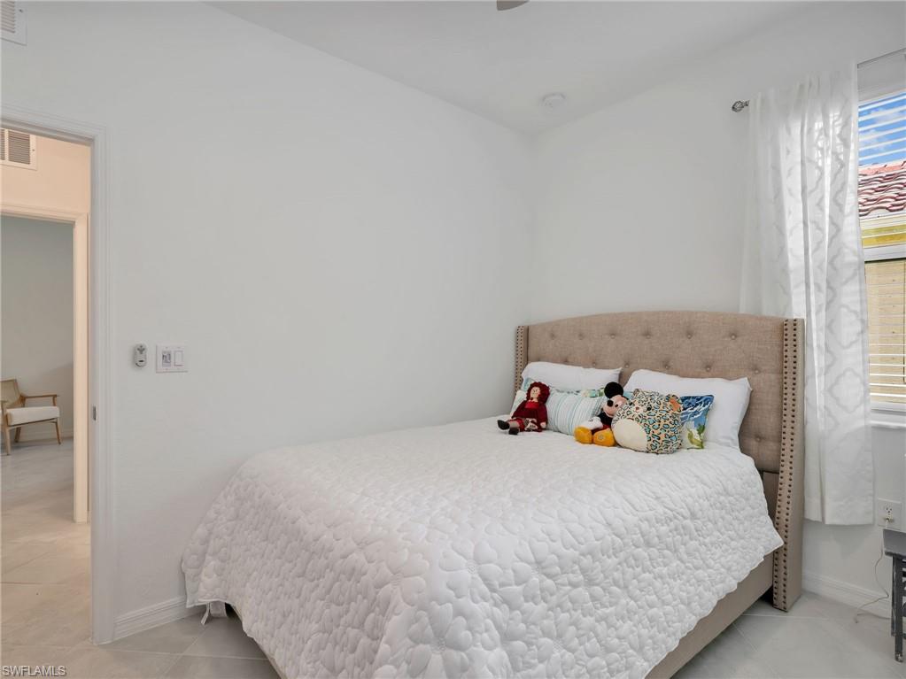 Bedroom featuring a textured upholstered headboard, light-toned tiled flooring, baseboard trim, and a window with blinds and sheer curtains