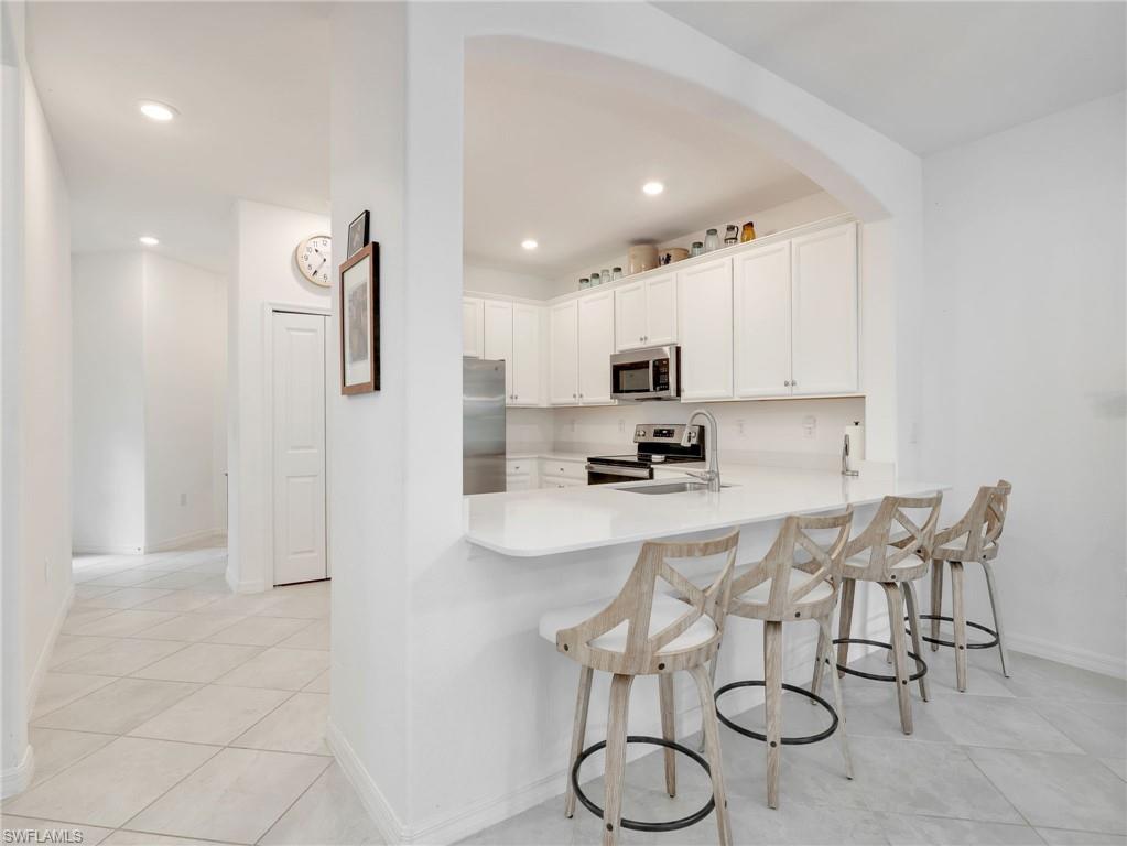 Kitchen featuring an arched passthrough, recessed lighting, white cabinetry, stainless steel appliances, and a breakfast bar with seating for four